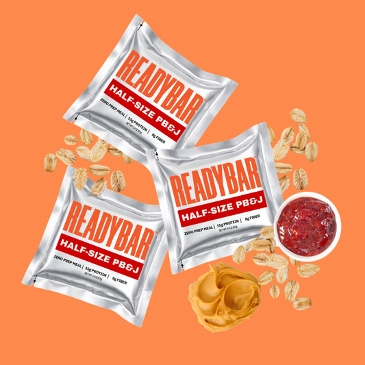 Three READYBAR Half-Size PB&J meal bars on an orange background with creamy peanut butter, oats, and strawberry jelly.